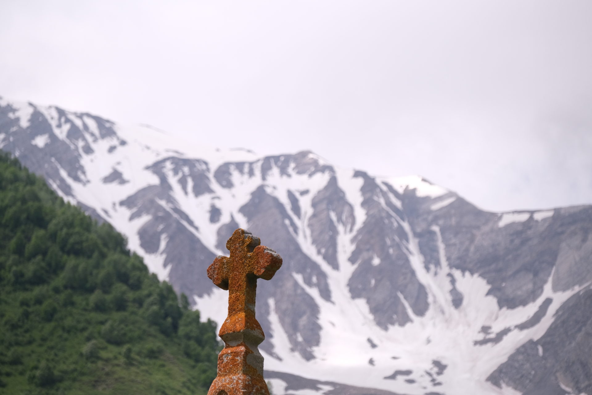 A cross in front of green forest and a snowy mountain, just outside of Kazbegi, Georgian elections.